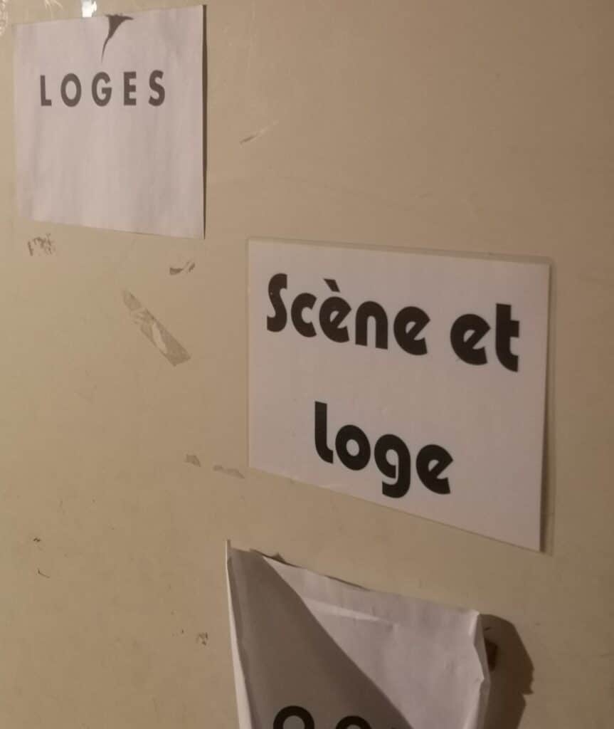 Beige wall with a white poster that says LOGES in bold letters (left) and a second sign nearby showing part of the phrase 'Scène et' (right).